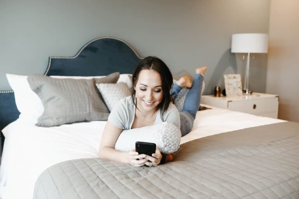 Woman laying on bed smiling at phone 