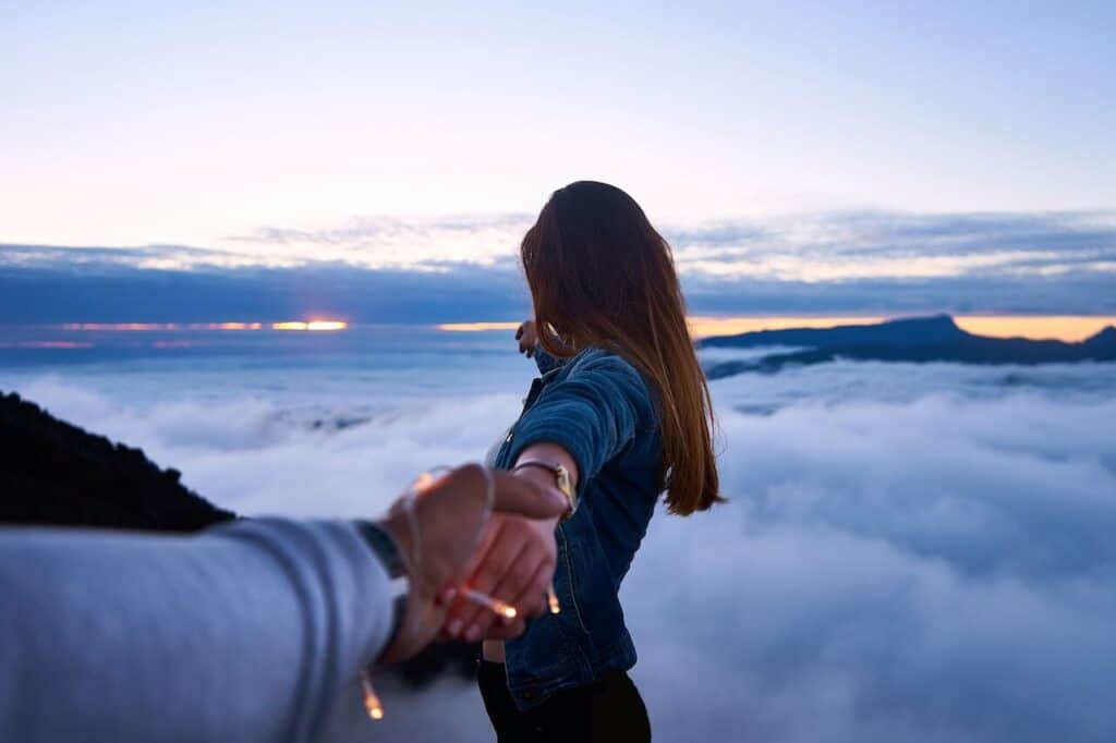girl looking over clouds holding a mans hand