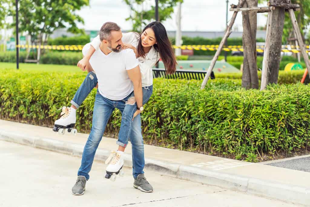 Man giving woman a piggy-back ride while she wears roller skates.  