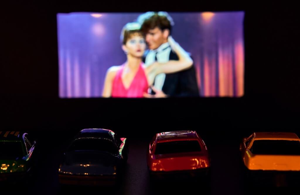 picture of cars parked in front of a drive in movie theater screen. 