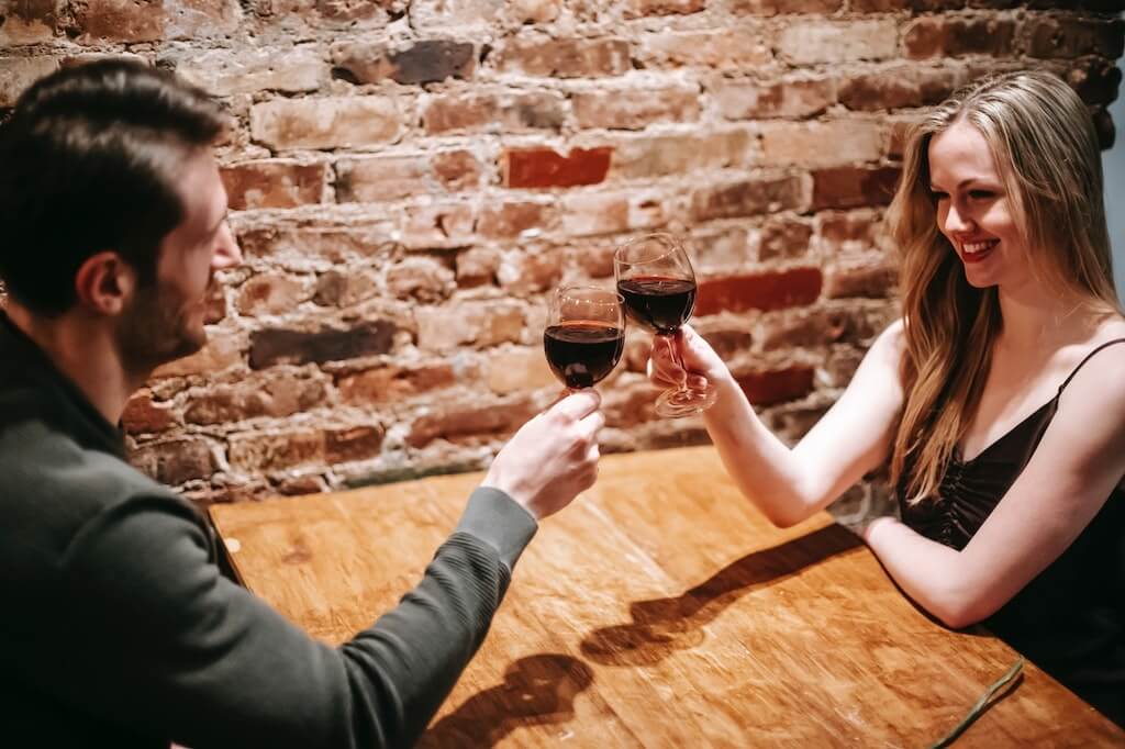 couple smiling while sitting at table clinking glasses of wine. 