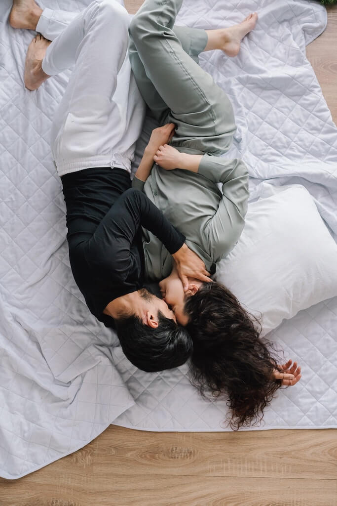 Couple laying on a blanket on the floor, with their faces pressed together.