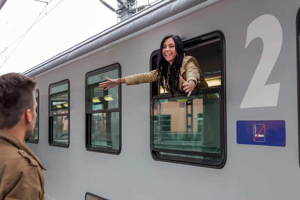 woman leaning out of a train window, reaching her arms out for a goodbye to a man. 