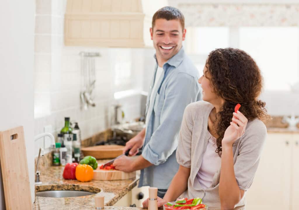 image shows a couple laughing and cooking together in their kitchen. 