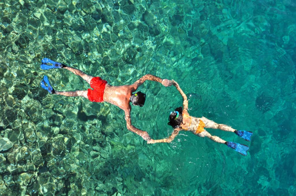young couple snorkeling in clear tropical water over coral reef. 