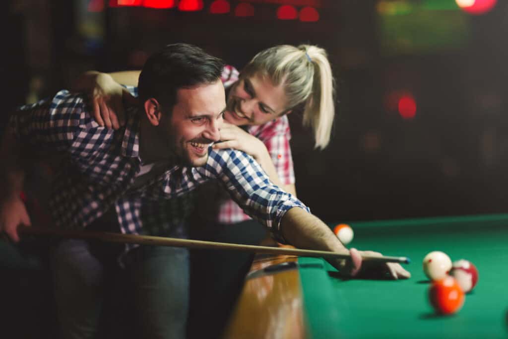 image shows a couple shooting pool while laughing and having a good time. 