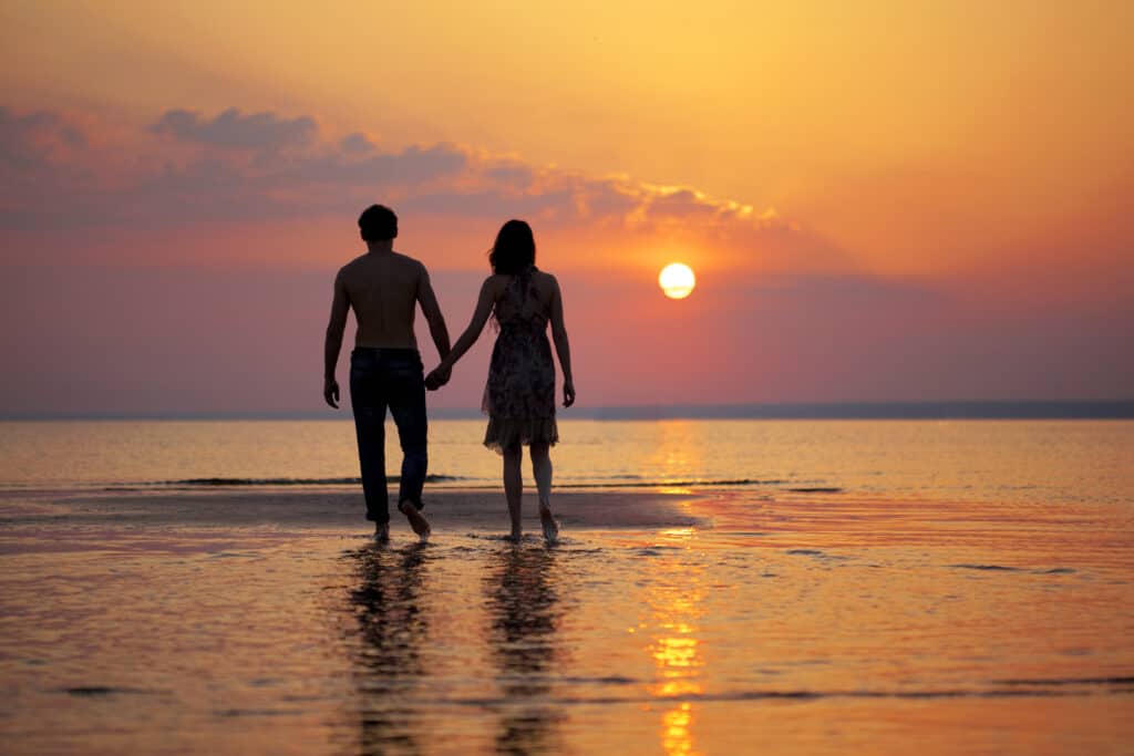 a couple holding hands walking on the beach during the sunset. 