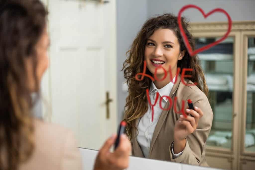 woman writing "Love you" in lipstick on a mirror for her boyfriend. 