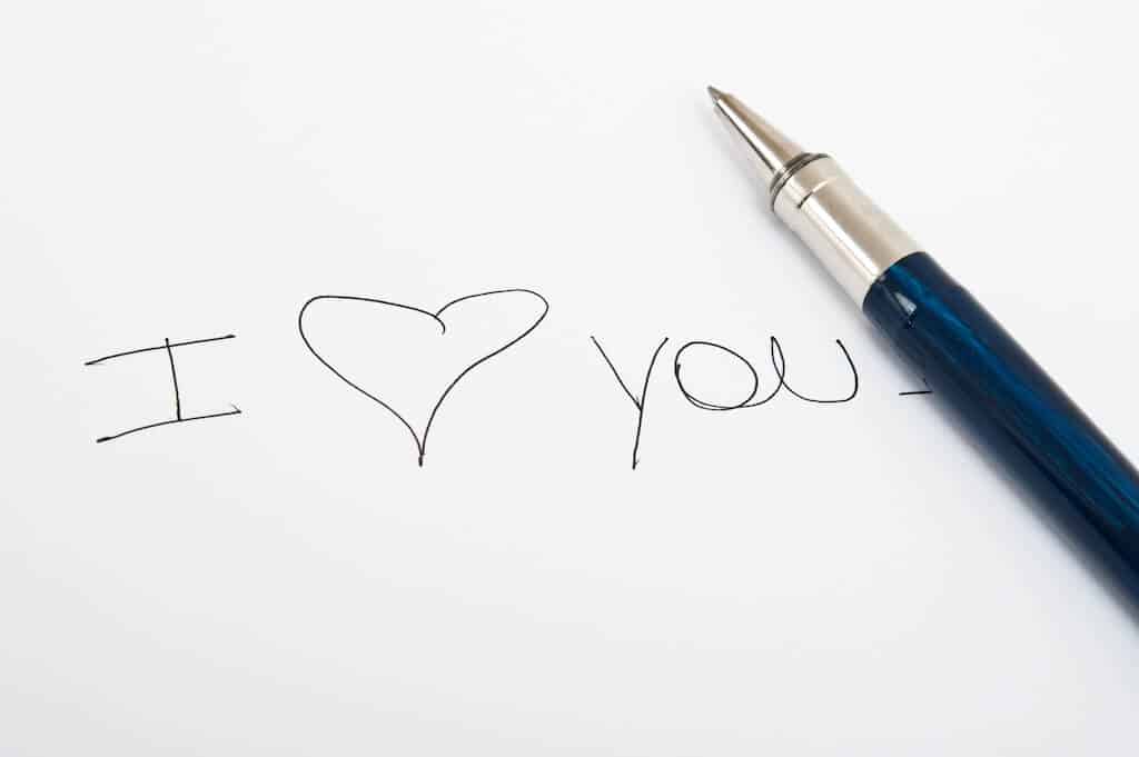 a pen laying next to written "I love you" on paper.