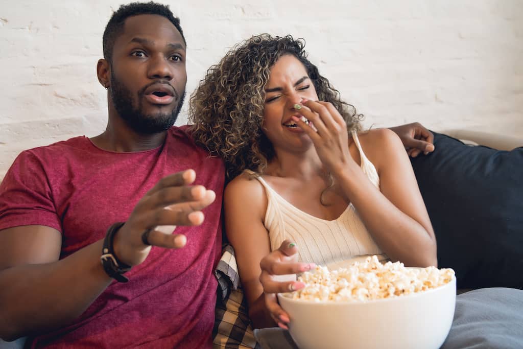 couple watching TV with popcorn while woman is laughing. 