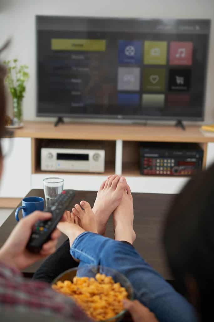shot of couples feet propped on a table, watching TV together.